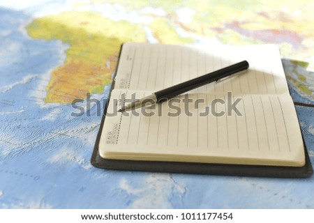 Pen on the notebook, open book placed on the map