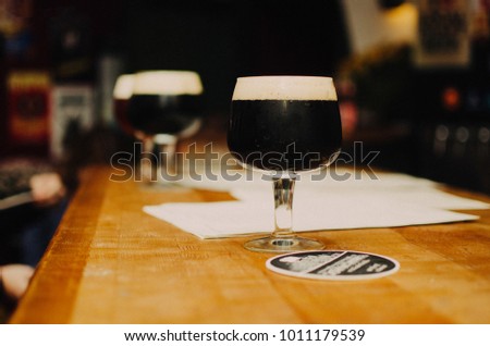 a glass with a dark beer, in the background, two more glasses are blurry. party at the bar