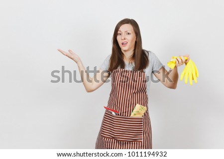 Young sad upset tired shocked housewife in striped apron with cleaning rag in pocket isolated on white background. Housekeeper woman holds smell yellow gloves in spreading hands. For advertisement