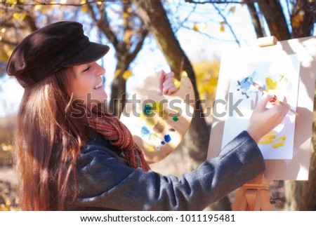 Girl with palette in hand sketches on white paper
