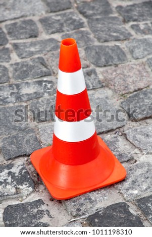 The top view on cone zone, orange road cone with white stripes on the road from paving stones.