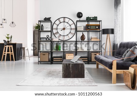 Laptop on black table and wooden dark sofa in manly flat interior with round clock on the wall and stools at kitchen island Royalty-Free Stock Photo #1011200563