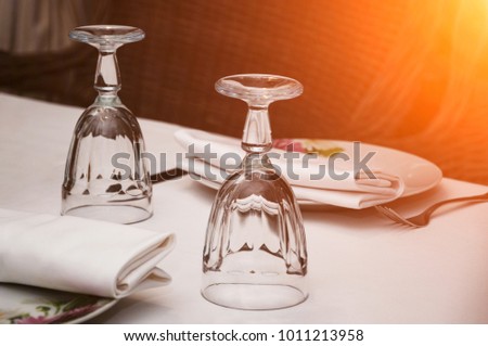 Empty inverted glasses on a table with white tablecloth in a restaurant. Toned