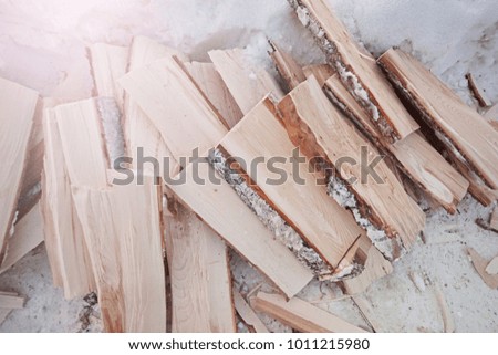 A pile of wooden firewood on the snow, prepared for the winter. Chopped logs.