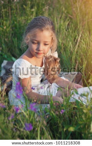 Little girl with a book in her hands on a meadow in a summer sunny day.