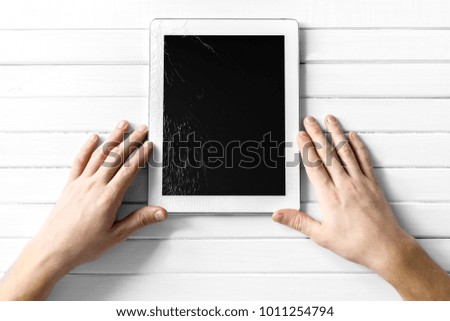 Broken electronic device screen on a white wooden background. Broken tablet screen.