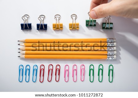 Person's Finger Arranging The Pencils With Row Of Pins Rubber And Pen On White Background Royalty-Free Stock Photo #1011272872