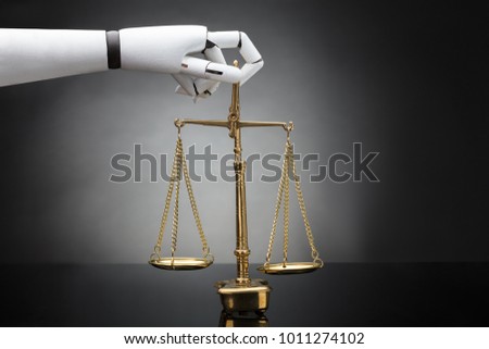 Close-up Of A Robot's Hand Holding Justice Scale On Grey Background Royalty-Free Stock Photo #1011274102