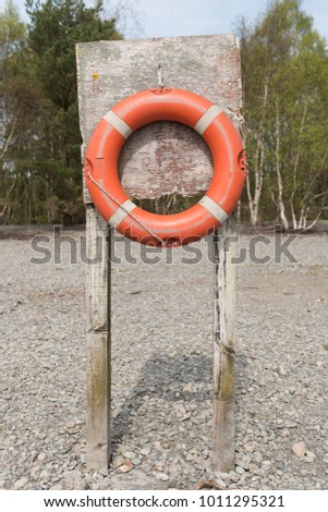 An old orange rustic life buoy attached to a weathered wooden post,  on a lake beach with a forest background