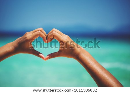 female hands in heart shape on sea beach at day time background, Summer season