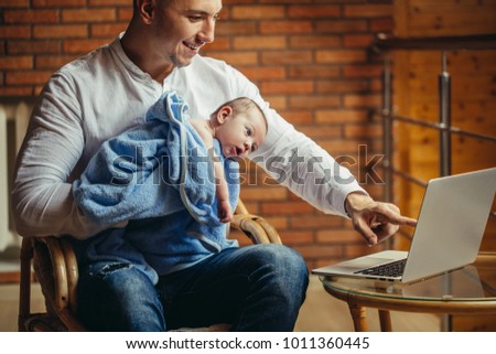 man working at desk at home with laptop, holding cute babys, looking at screen, little helper, benefits of freelancing