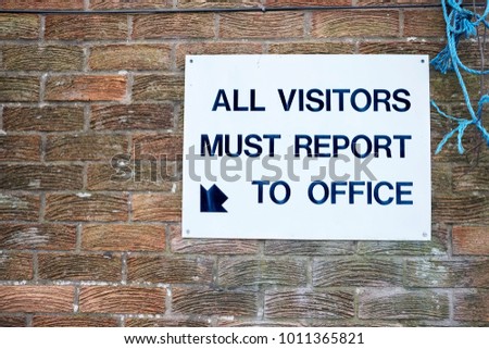 All visitors must report to office sign fixed to brick wall at workplace