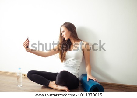 sports woman sitting on floor and making selfie on smartphone in fitness gym