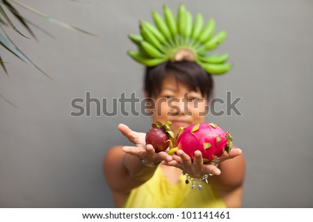 Woman holding fresh fruit in hands in focus and bananas on head blurred