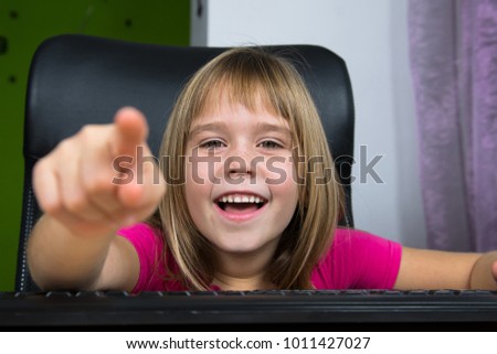 Little girl sitting at the computer and pointing to the screen.