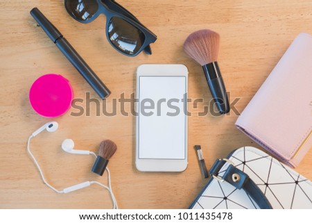 Top view of blank screen Smartphone and  Women bag and lady stuff with copyspace on wooden background