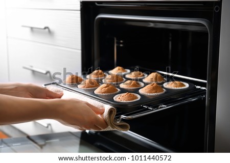 Woman taking baking tray with cupcakes from oven Royalty-Free Stock Photo #1011440572