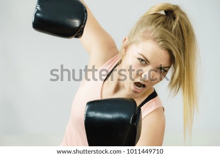 Sporty woman wearing black boxing gloves, fighting. Studio shot on grey background.