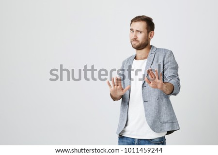 Attractive bearded man makes frightened gesture with palms, defends himself from someone, asks to stop it immediately. Guy says stay away from me, shows stop sign. Body language concept Royalty-Free Stock Photo #1011459244