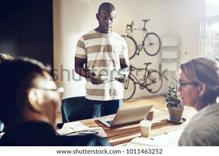Young African man giving a presentation to coworkers sitting together around a table in a modern office