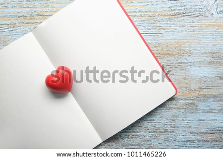 Notebook with red heart on wooden background