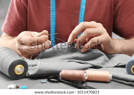 Tailor sewing button on fabric at table in workshop