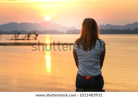Young woman standing and hand up with beautiful nature sunset on lake and mountain with warm light as vacation or relax or happy concept