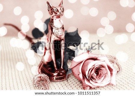 Statuette of Bastet with a beautiful pink rose on a gold grid with bokeh effect 