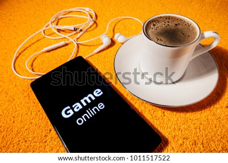 Games online concept with fragrant coffee. In the picture there is a smartphone and headphones as a symbol of gaming applications on the Internet.