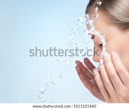 A woman is washing her face with cold water, cleaning skin after makeup, using anti acne or anti aging agent, pampering and beauty care concept, over blue clear background Royalty-Free Stock Photo #1011525460