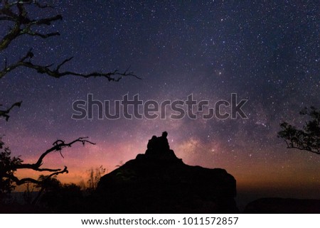 Landscape with Milky Way. Night sky with stars and silhouette of a sitting happy love couple on the hill.
