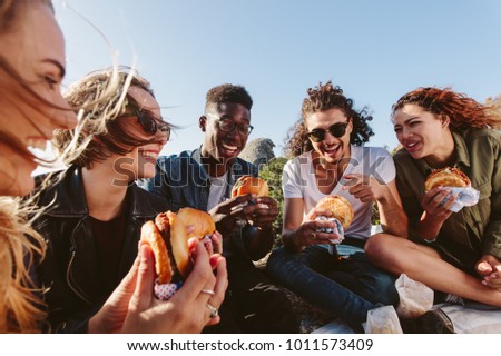 Young people having summer picnic and eating together sitting on mountain top. Happy friends on mountain top having a picnic on a summer day. Royalty-Free Stock Photo #1011573409