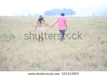 man and women holding hand and walking in grass field