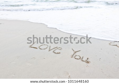 The hand writing love you on the white sand beach and white wave of sea for lover in Valentine's Day