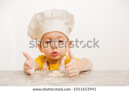 Details of children's hands kneading dough. Cheerful cook child boy in a cap prepares burritos or pizza