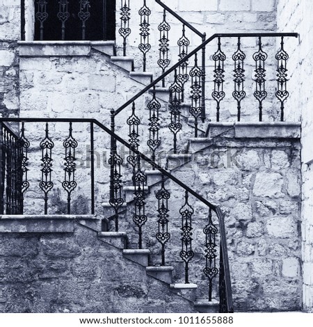 Ancient stone staircase with ornate wrought handrail, old monochrome film effect
