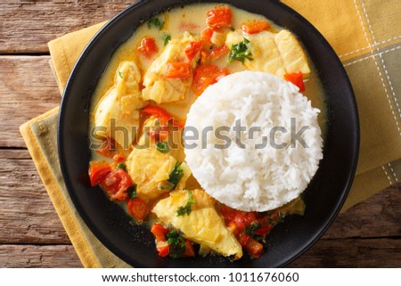 Stew fish with sauce of cilantro, onions, tomatoes, bell peppers and coconut milk with garnish of rice close-up on a plate. Horizontal top view from above
