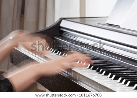 Wooden black piano with keyboard and female hands of musicians motion blurred, with blurred background