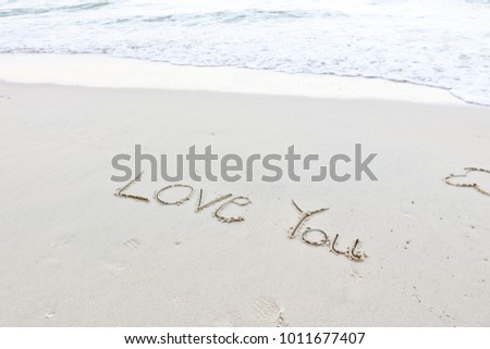 The hand writing love you on the white sand beach and white wave of sea for lover in Valentine's Day