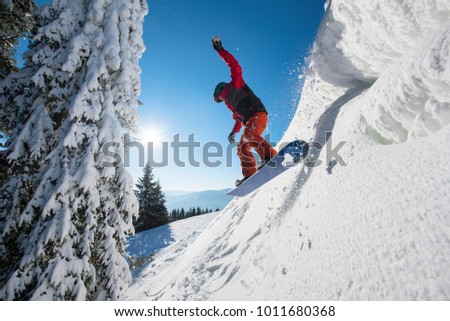 Motion picture of a snowboarder flying in the air while riding the snowy slope in winter. Blue sky, sun, forest and mountains on the background copyspace sport extreme people lifestyle concept