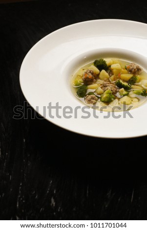 vegetable soup with meatballs and broccoli in a white plate
