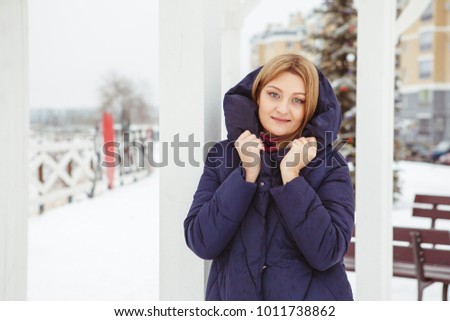 Beautiful blonde girl with blue eyes in winter outdoors, portrait. A young girl looks into the camera and smiles. Close-up