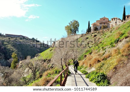 walkers walking Walk along the footbridges of the Tagus River, In the background the National Tourism Parador of Toledo, path of the coastal edge of the cliffs of the Tagus in the city of Toledo,