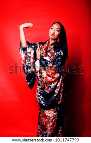 young pretty geisha on red background posing in kimono, oriental people concept close up