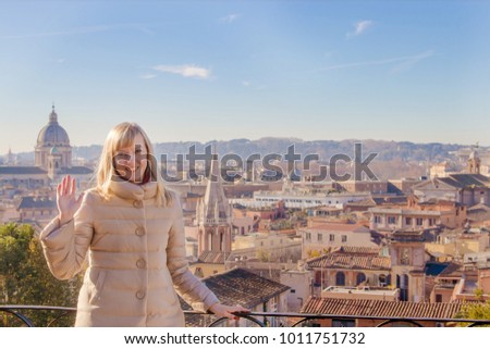 Portrait of a happy young blond woman waving her hand against the background of Rome Italy.