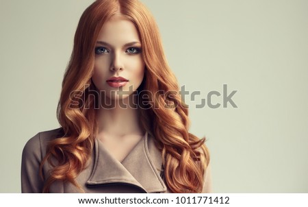 Red head  girl with long  and   shiny wavy hair .  Beautiful  model woman with curly hairstyle .