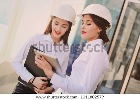 Two young cute girls in business clothes and white construction helmets discuss a business plan or contract