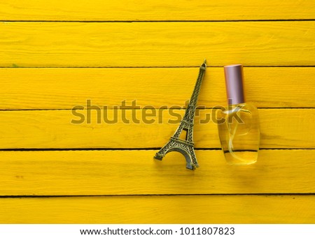 A perfume bottle and a souvenir statuette of the Eiffel Tower on a yellow wooden background.
