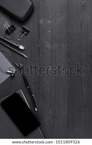 Black wooden table with smartphone and work accessories. Top view, copy space
