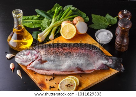 Fresh gutted trout on a wooden cutting board surrounded by ingredients for baking: olive oil, lemon, spring onions, garlic and spices. Top view Royalty-Free Stock Photo #1011829303